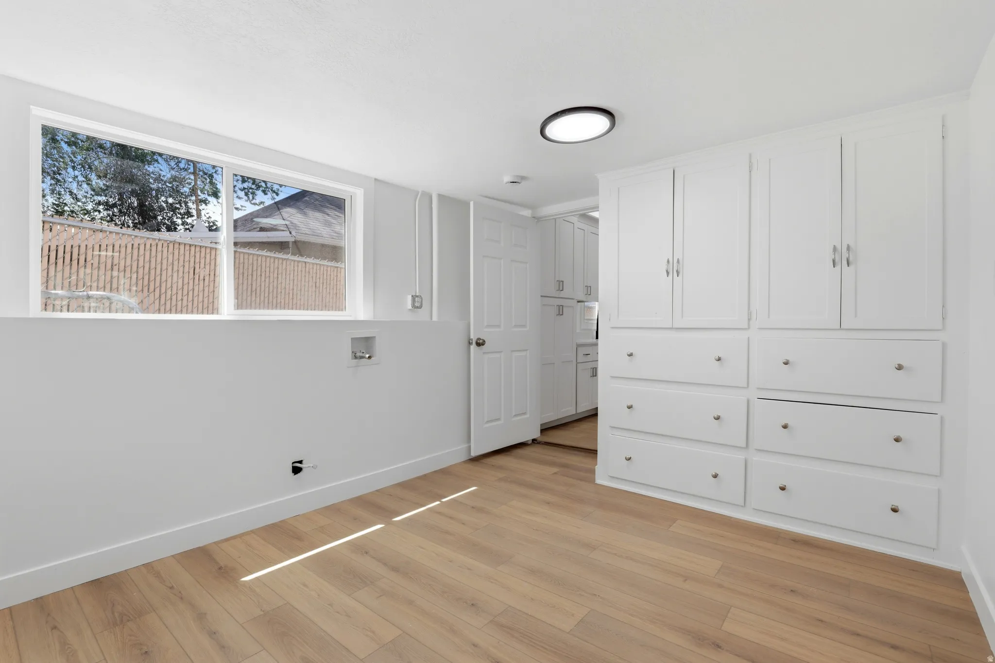 Bright utility space featuring light wood-finish flooring, a window, and built-in white cabinetry with drawers