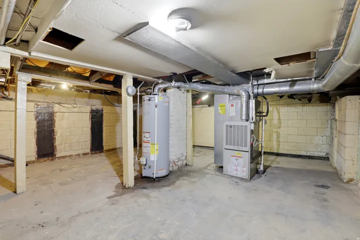 Concrete floor basement with exposed ceiling joists, cinder block walls, a water heater, and a furnace
