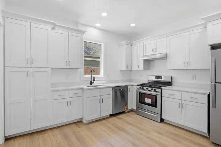 Kitchen featuring extensive white shaker cabinetry, stainless steel appliances, light-toned countertops, a matte black faucet, and wood-finish flooring