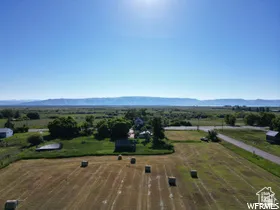 Aerial perspective showcasing agricultural fields with hay bales, a paved road, and distant mountain ranges under a clear sky