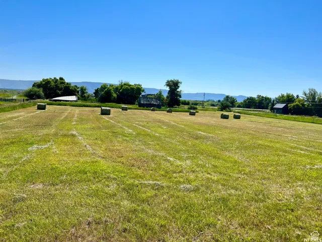 Expansive green field featuring multiple hay bales, a distant white barn, and a dark-roofed structure
