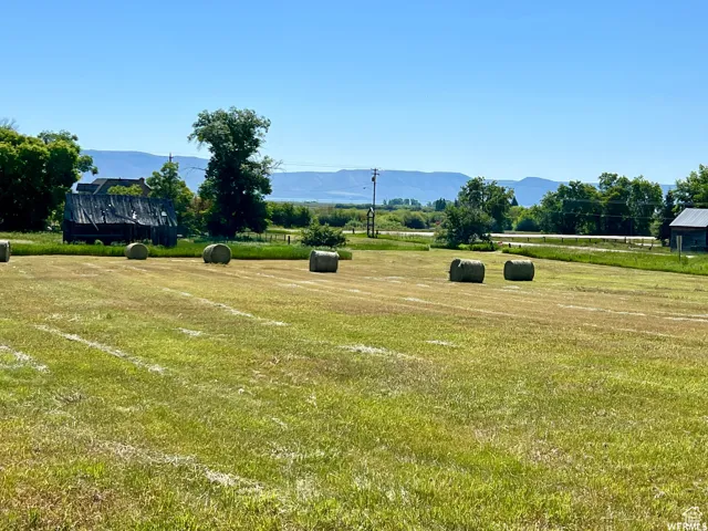 Expansive grassy acreage featuring multiple hay bales, a rustic barn structure, and mature trees, all set against a distant mountainous backdrop