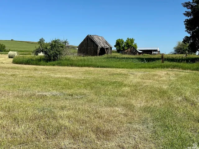Expansive green acreage featuring a weathered barn, additional outbuildings with metal roofing, and a hay bale