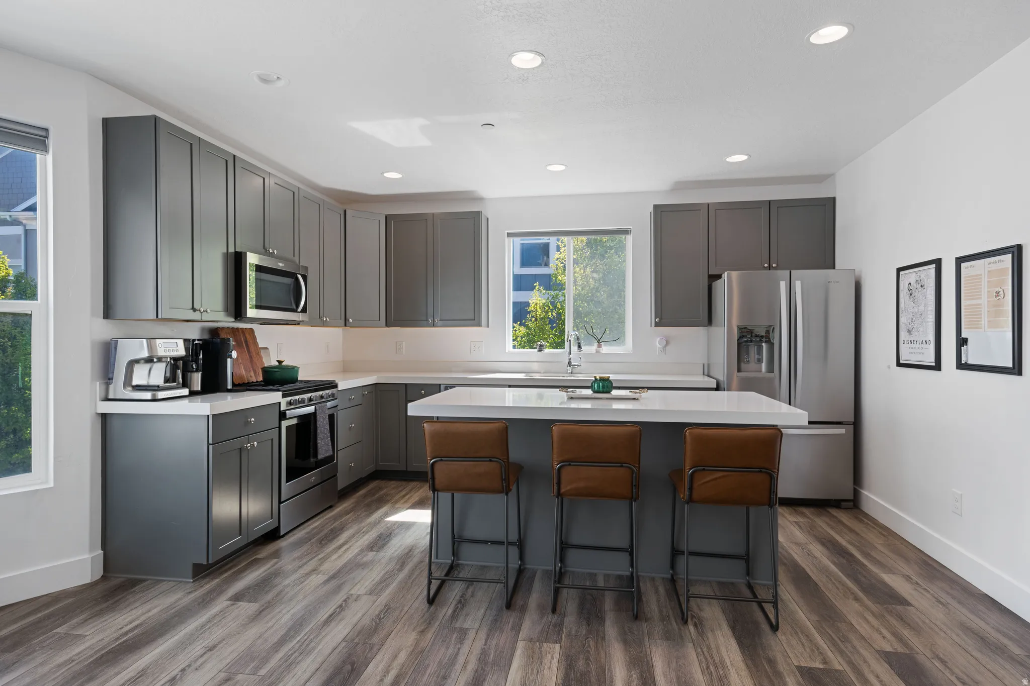 Contemporary kitchen featuring grey cabinetry, stainless steel appliances, light countertops, wood-finish flooring, and recessed lighting