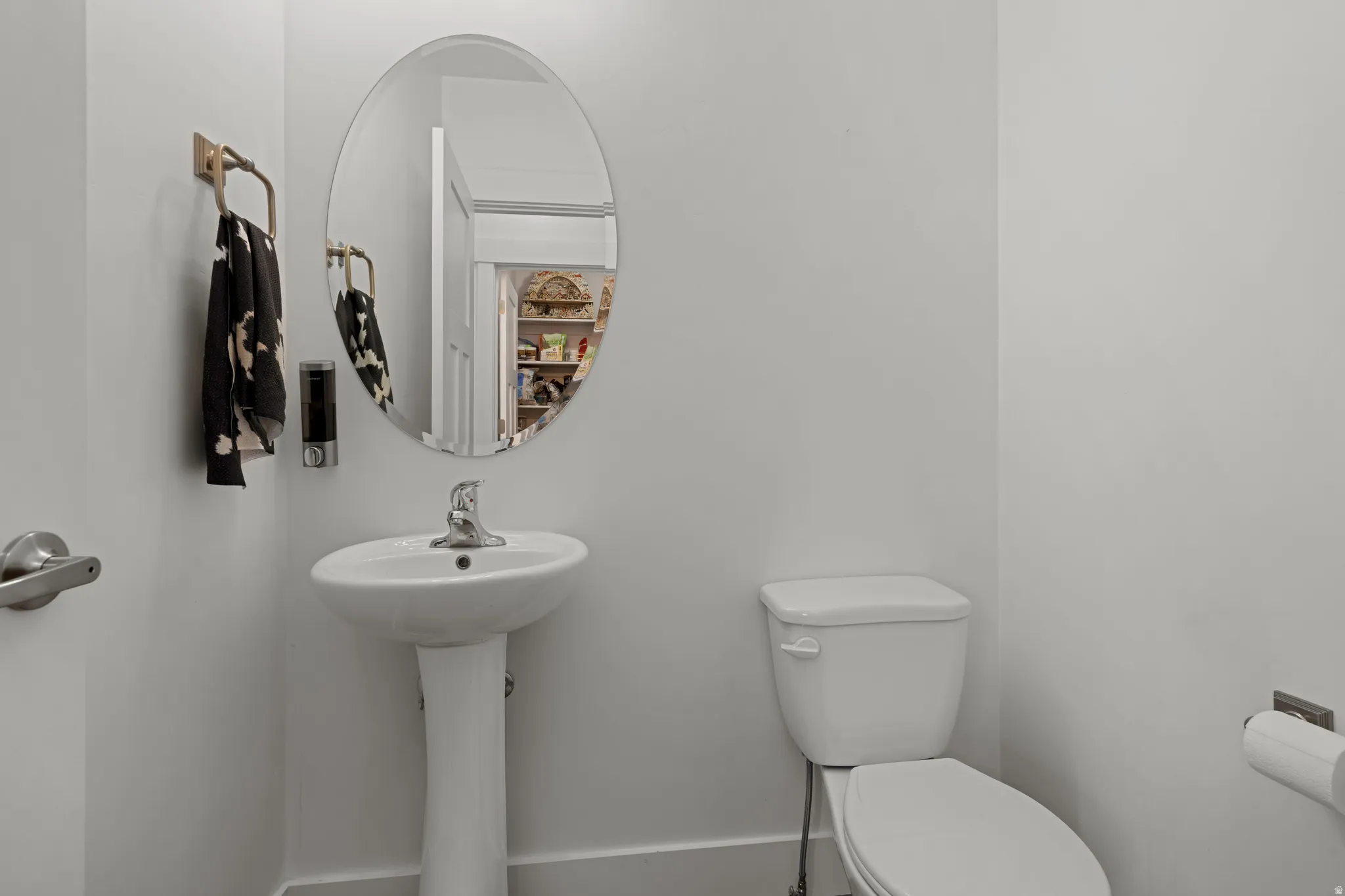 Pedestal sink with chrome faucet, an oval mirror, and a white toilet
