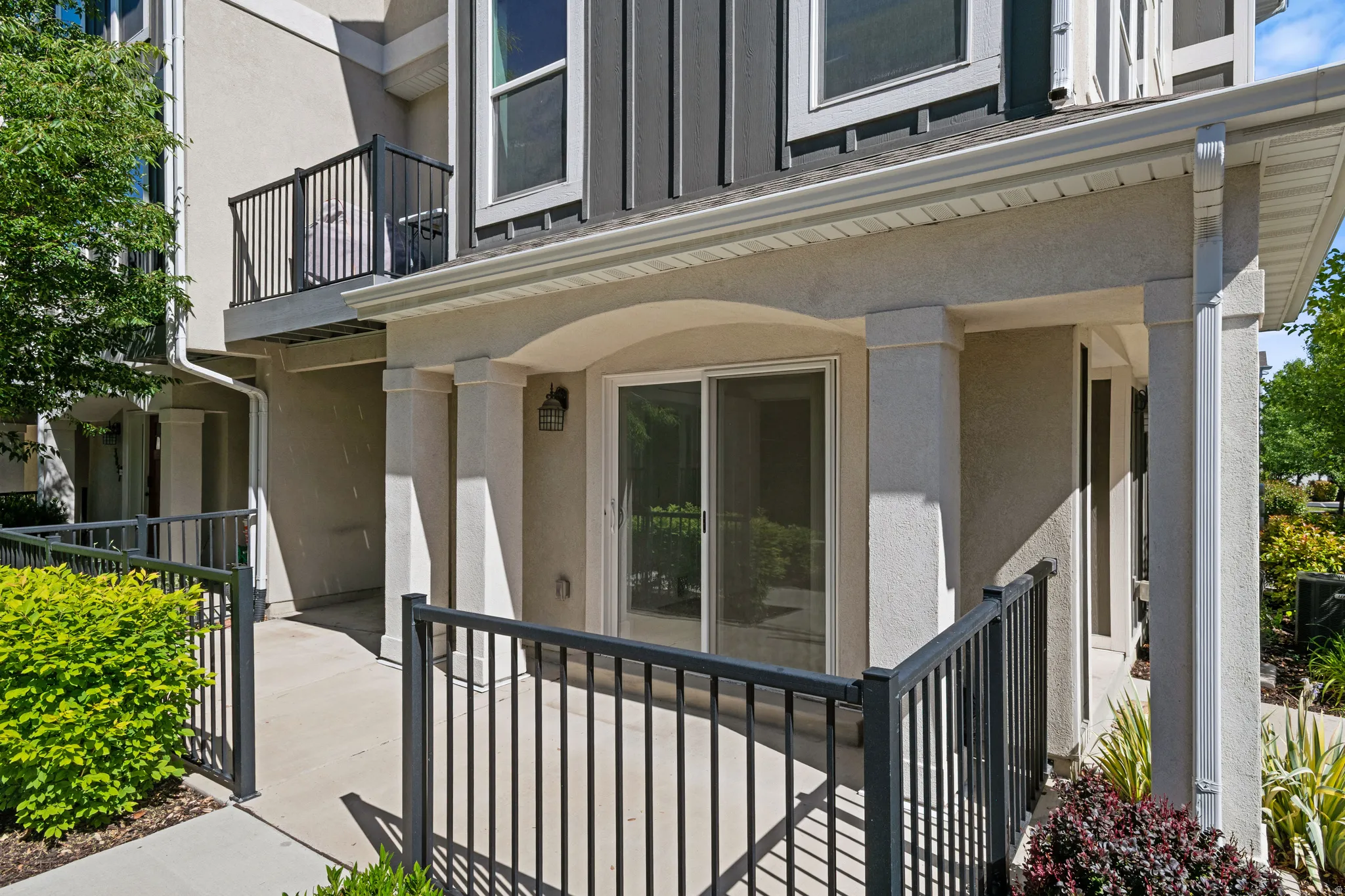 Ground-level patio featuring a sliding glass door entry, covered porch area, and black metal railings