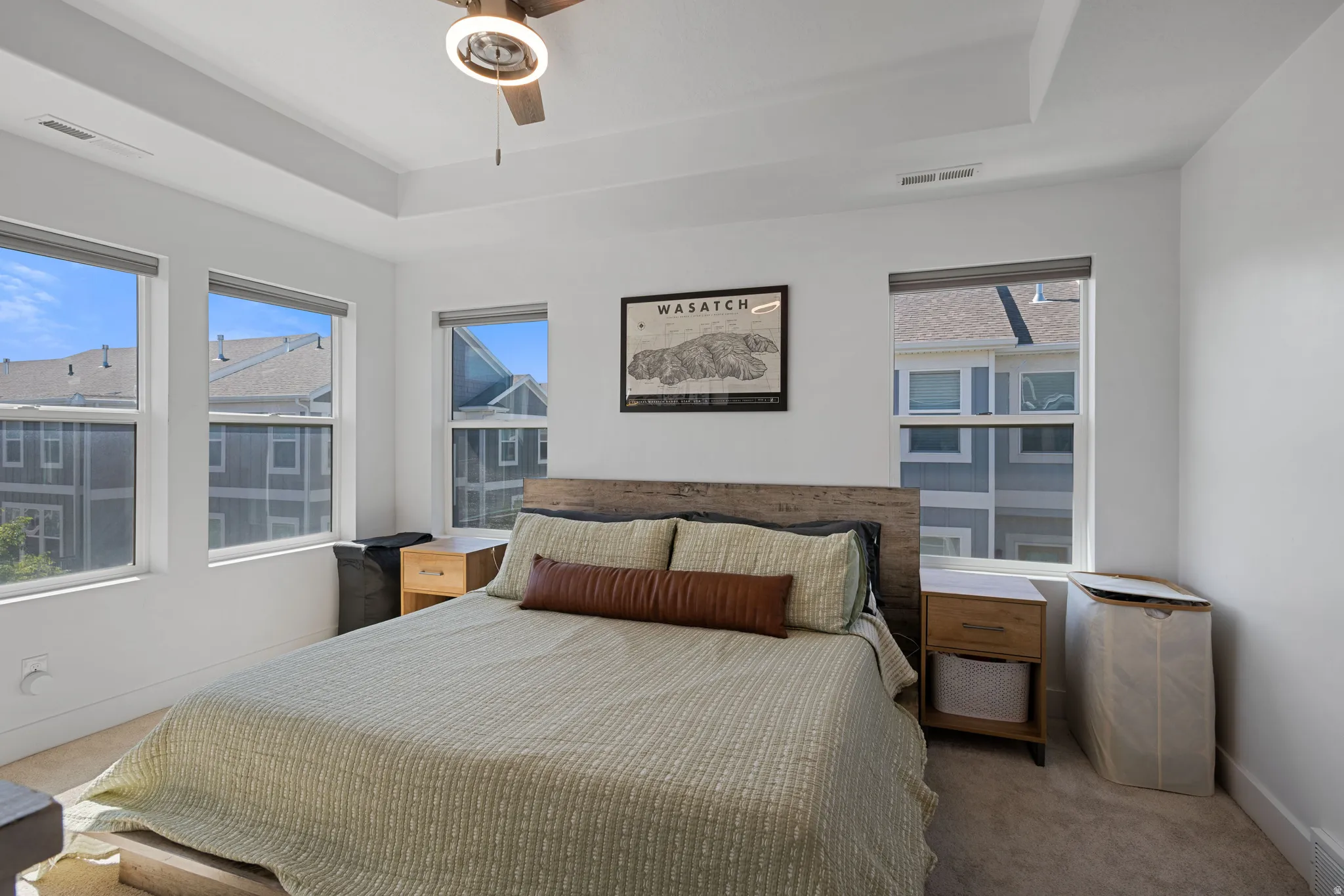 Bedroom featuring multiple windows, a tray ceiling, a ceiling fan, and carpet flooring