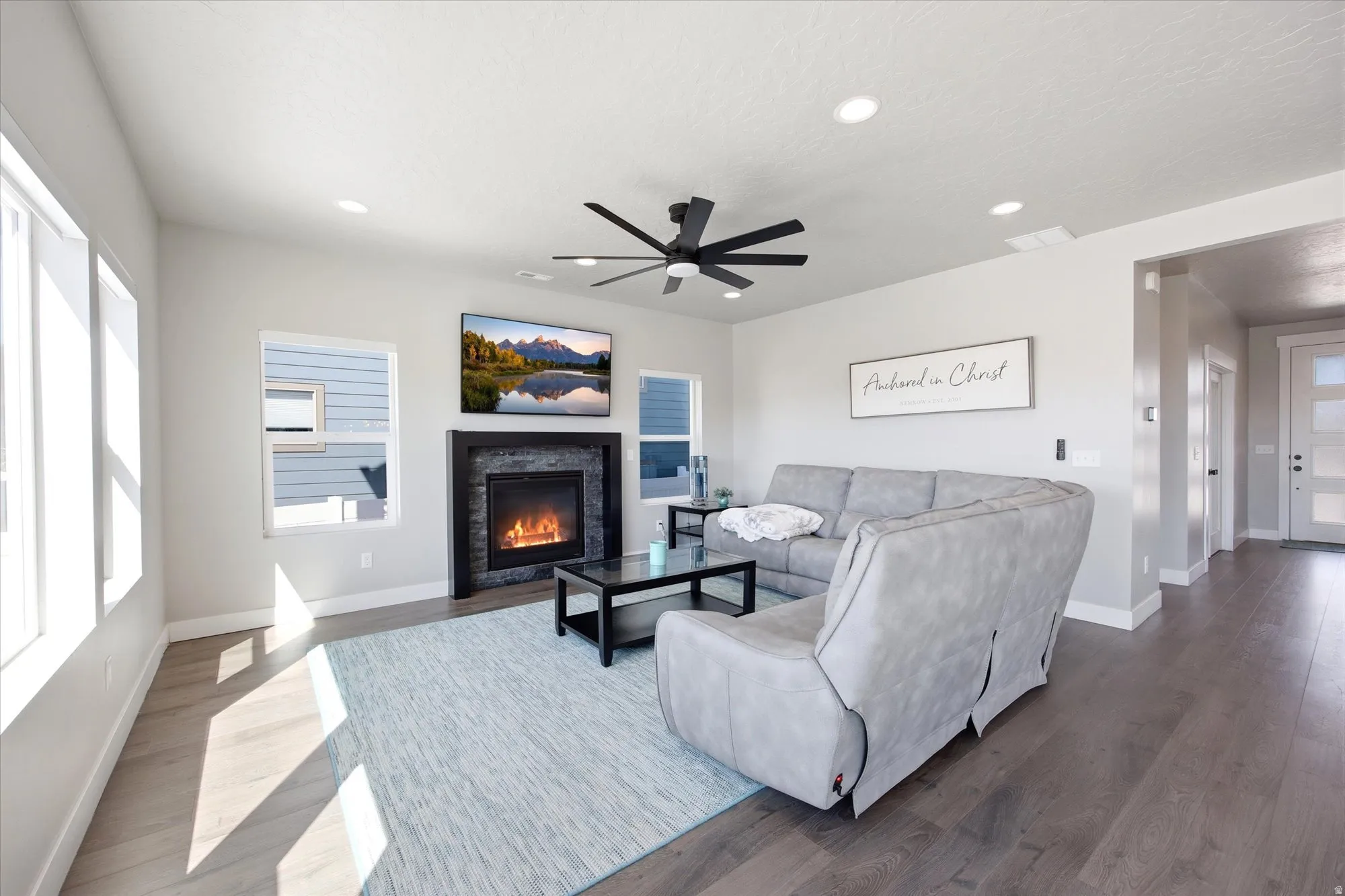 Living area featuring wood-finish flooring, a stone-clad fireplace, and recessed lighting