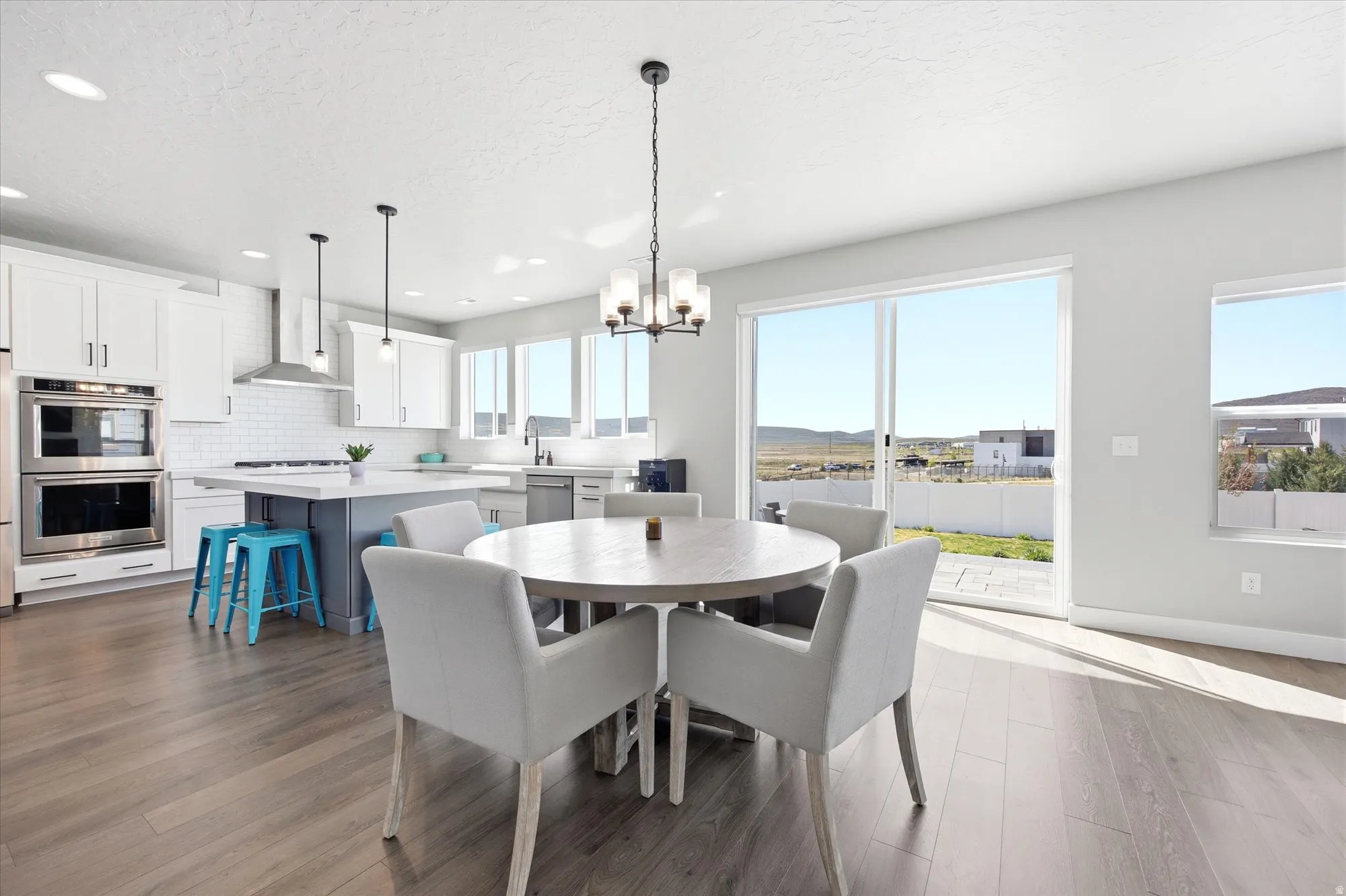 Open-concept living space featuring wood-finish flooring, a contemporary kitchen with white cabinetry and stainless steel appliances, a center island with a light-colored countertop, and a dining area with a chandelier