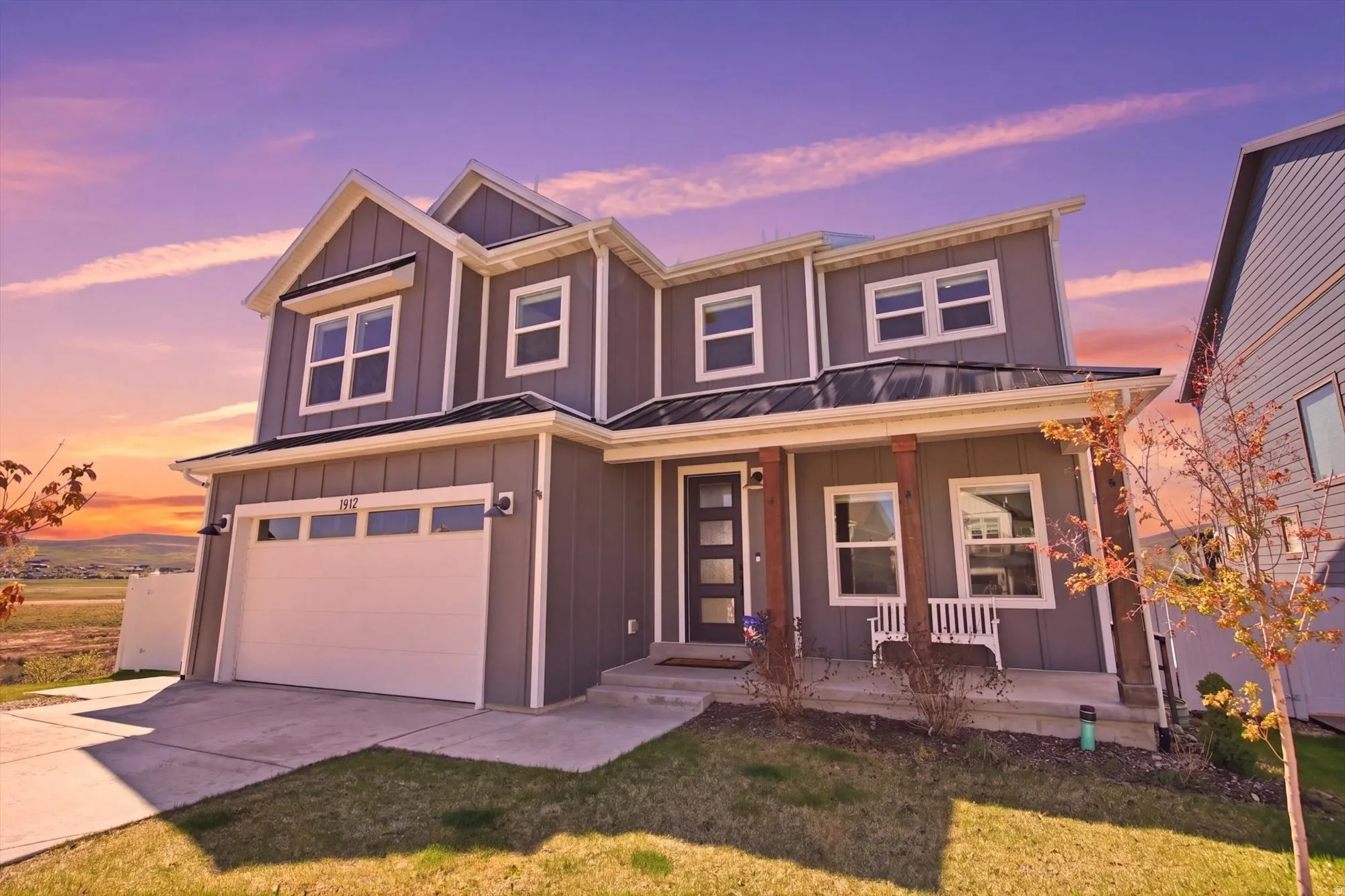 Contemporary multi-level residence featuring gray siding with white trim, a covered front porch with wood columns, an attached two-car garage, and a concrete driveway