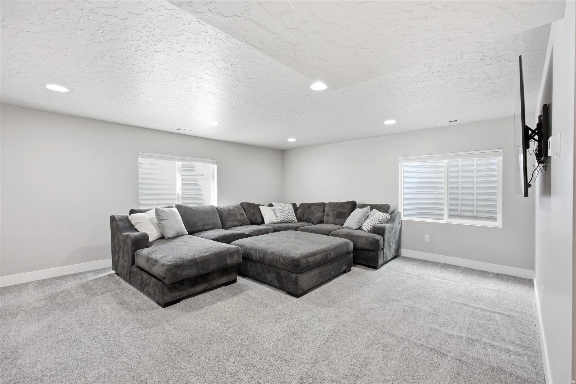 Spacious room featuring light gray walls, textured white ceiling, recessed lighting, and wall-to-wall light gray carpeting