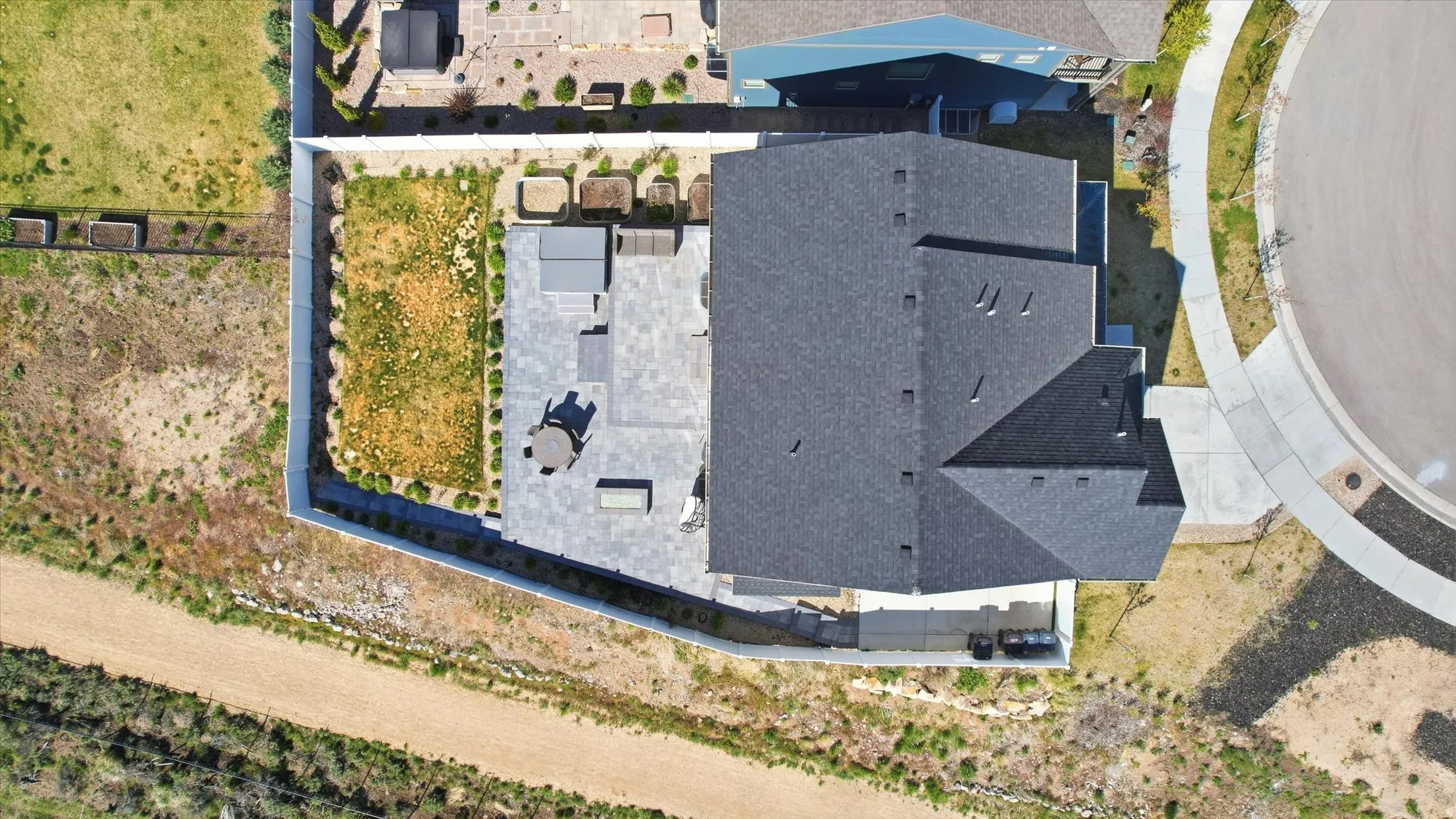 Aerial perspective of a contemporary residence featuring a dark shingle roof and a spacious paved patio