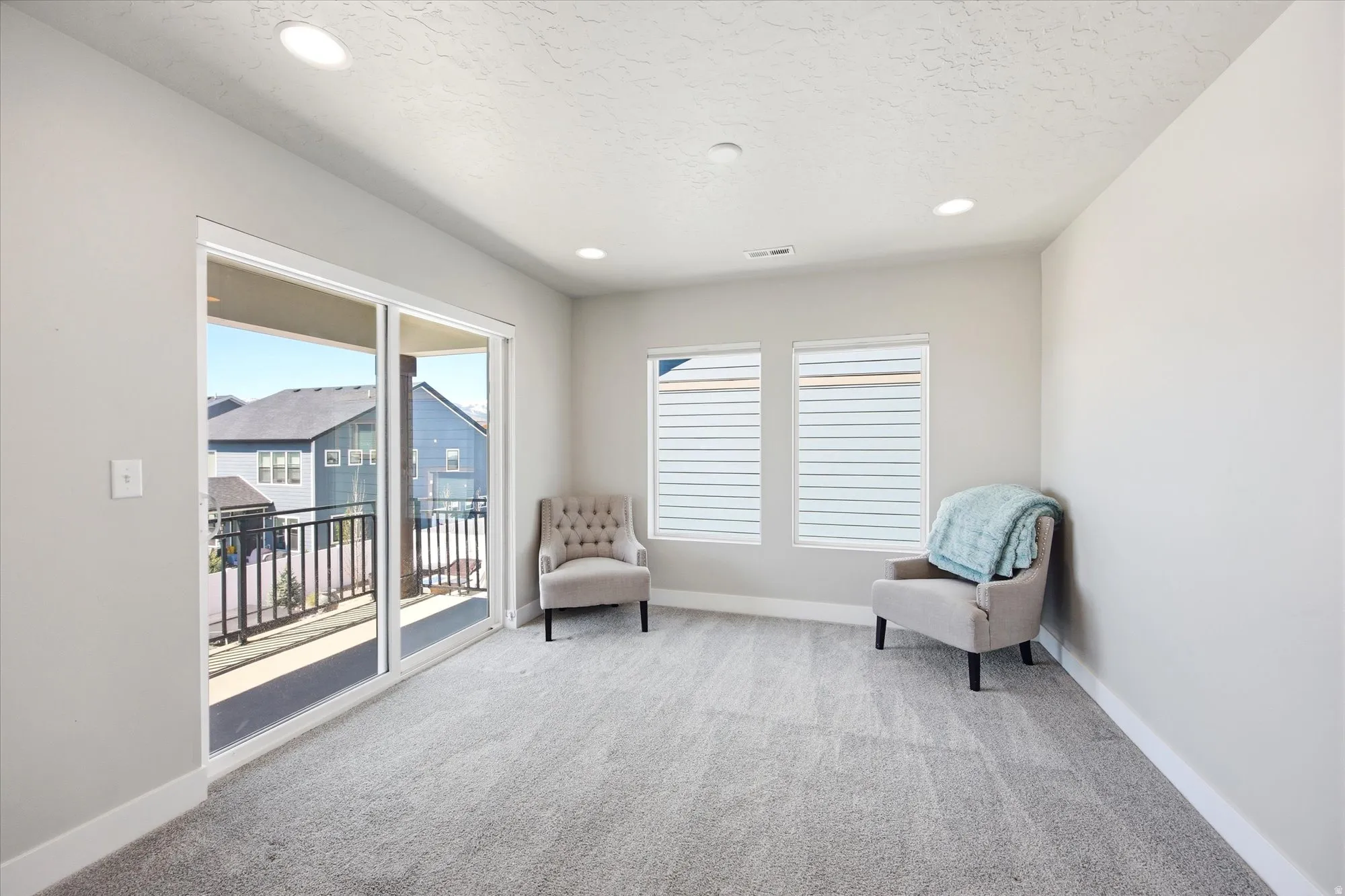 Spacious room with plush gray carpeting, recessed ceiling lighting, and a sliding glass door opening to a private balcony