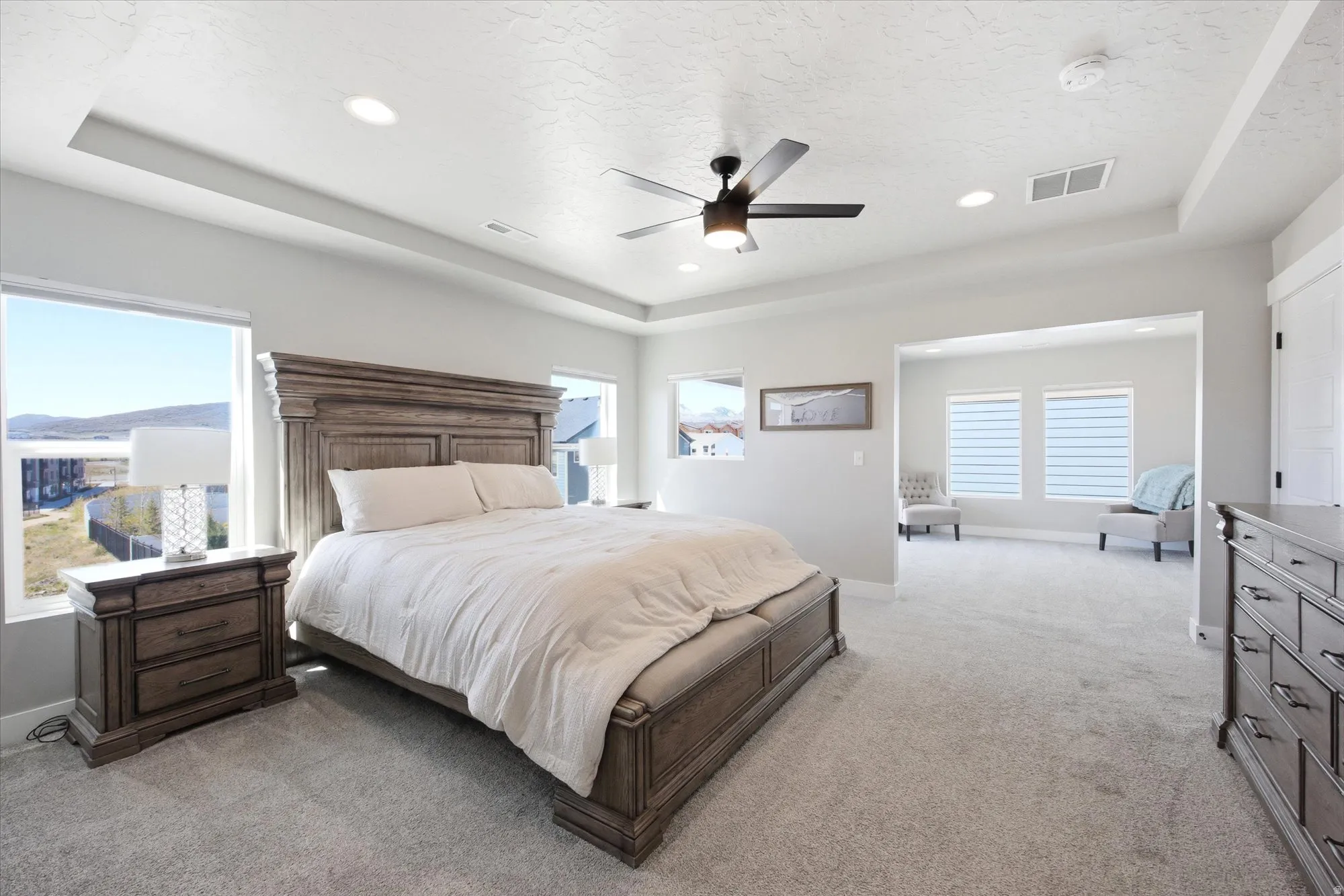 Recessed lighting and a ceiling fan illuminate this spacious bedroom featuring tray ceilings