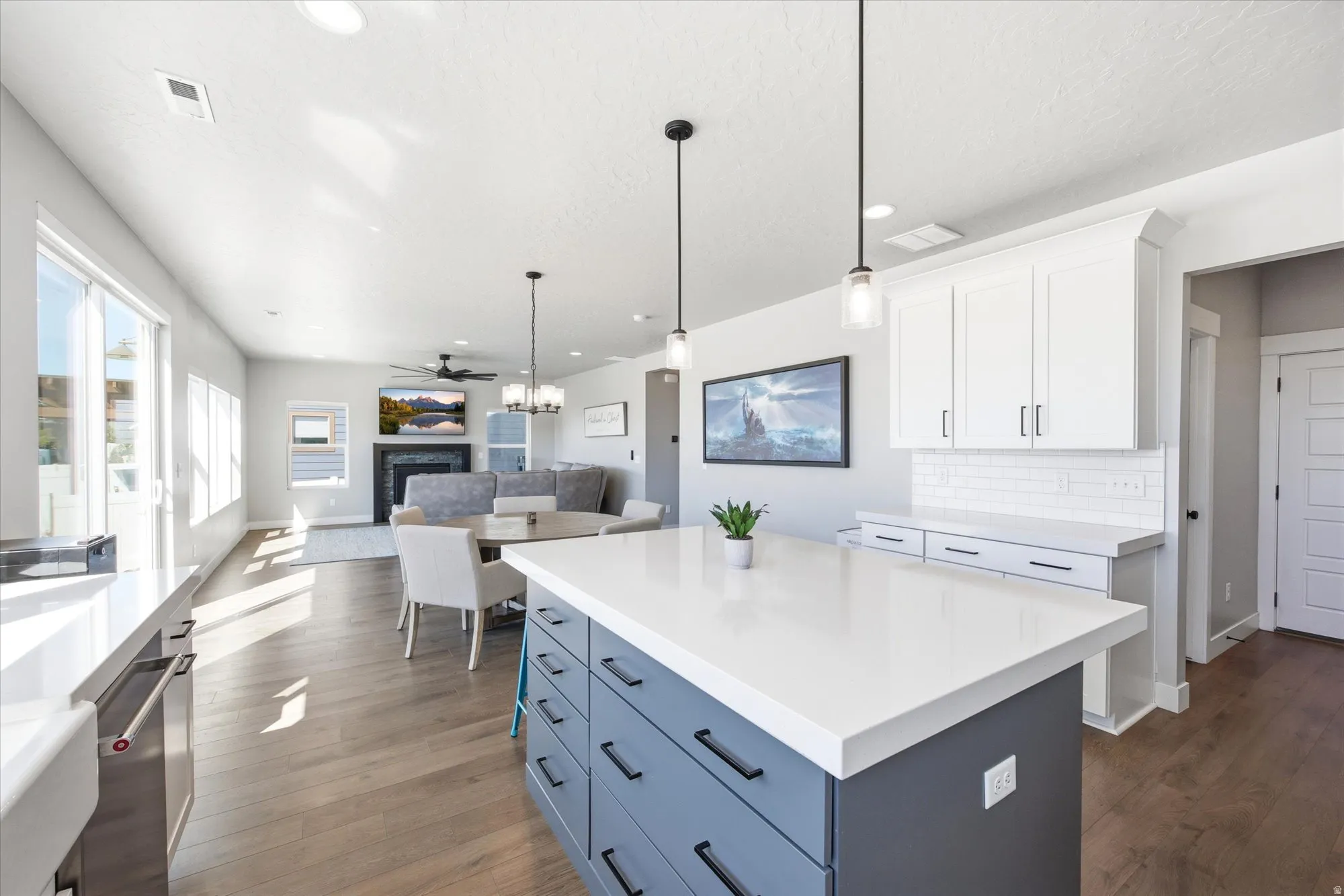 Open-concept living area featuring a kitchen island with pendant lighting, wood-finish flooring, white cabinetry, a subway tile backsplash, and sliding glass doors