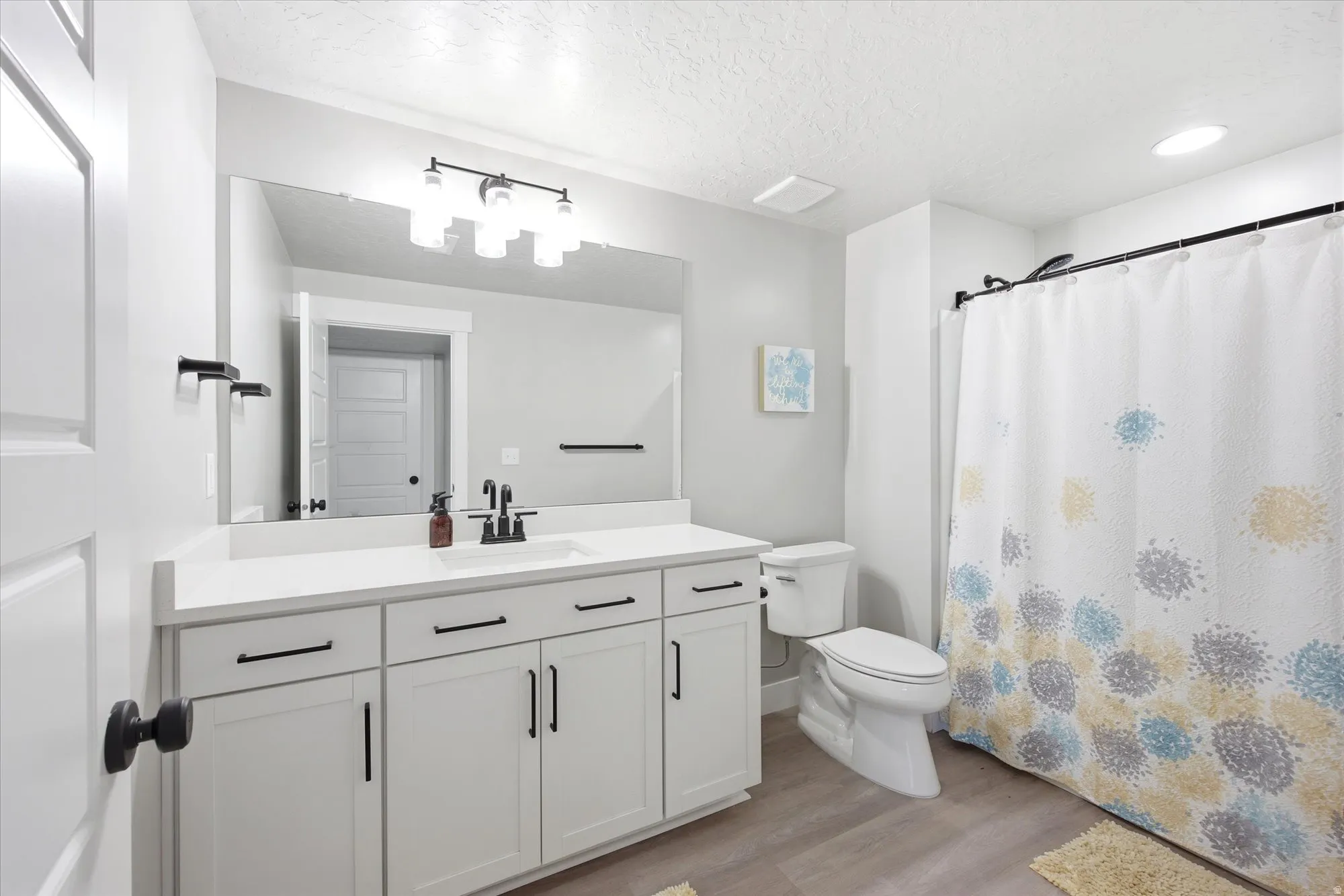 Bathroom featuring a white vanity with black hardware, a single basin sink, and a large wall-mounted mirror
