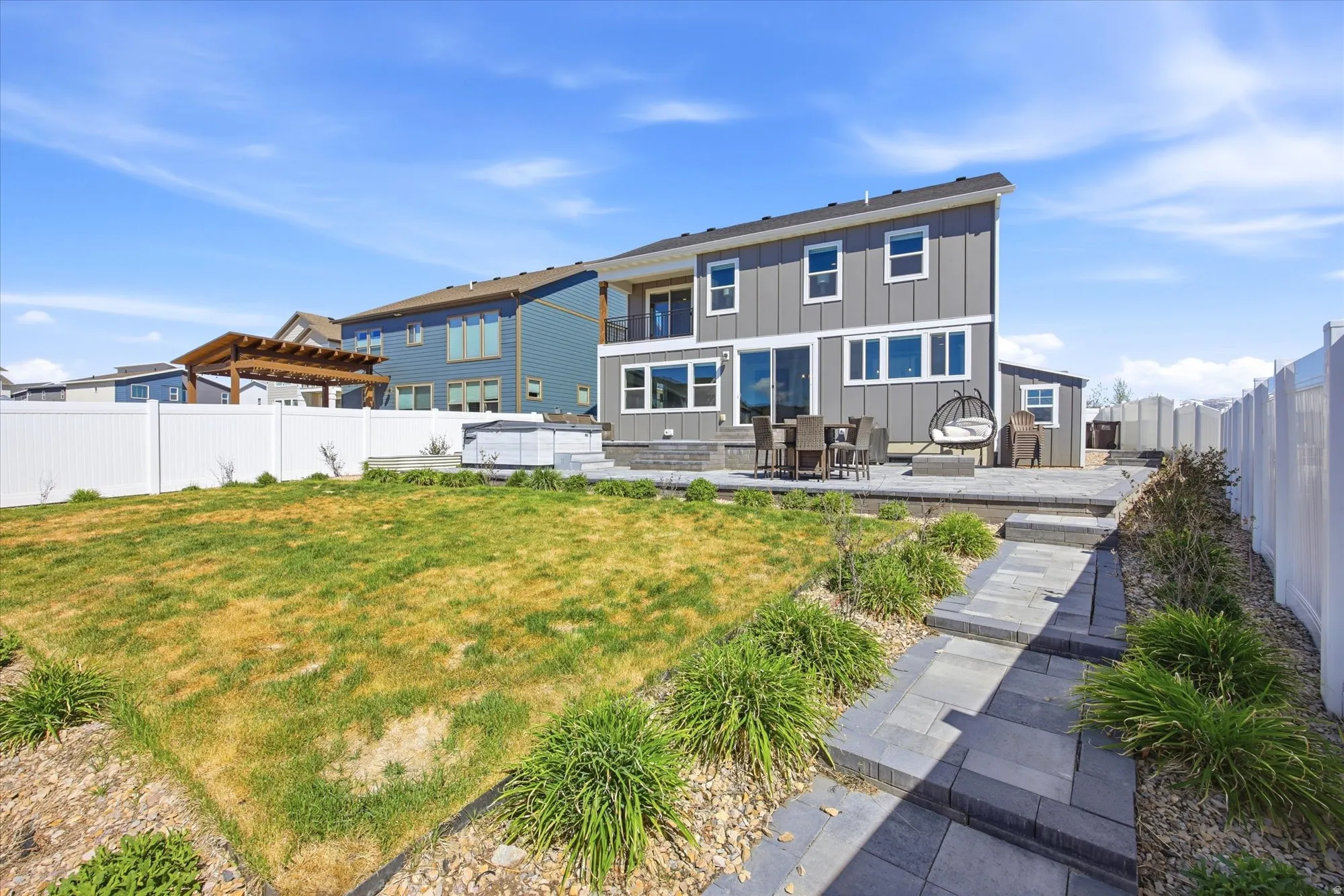 Expansive backyard featuring a multi-level paver patio, a white vinyl privacy fence, a detached shed, and a paved walkway with integrated landscaping