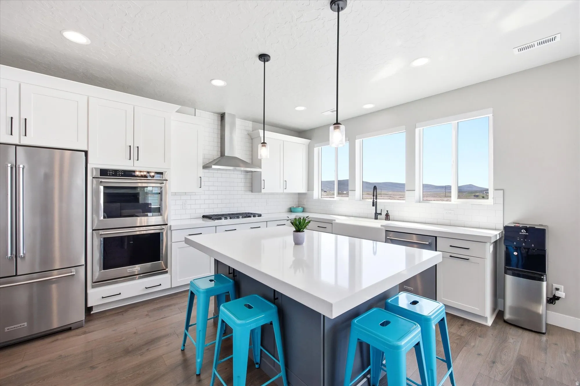 Contemporary kitchen featuring a large central island, white shaker cabinetry, stainless steel appliances, and wood-finish flooring