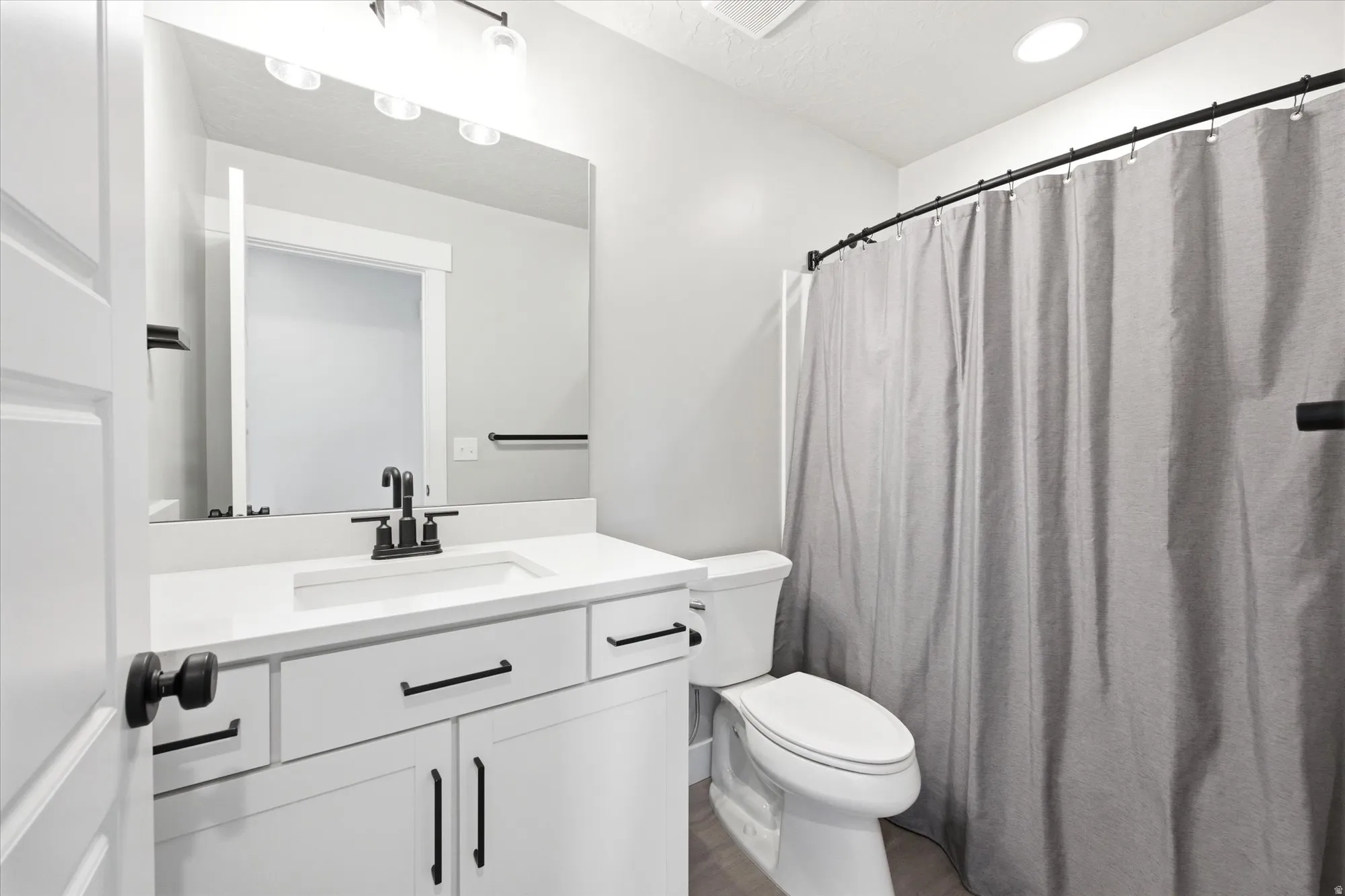 Bathroom featuring a white vanity with an integrated sink, black hardware, a wall-mounted mirror, and a shower with a curved rod