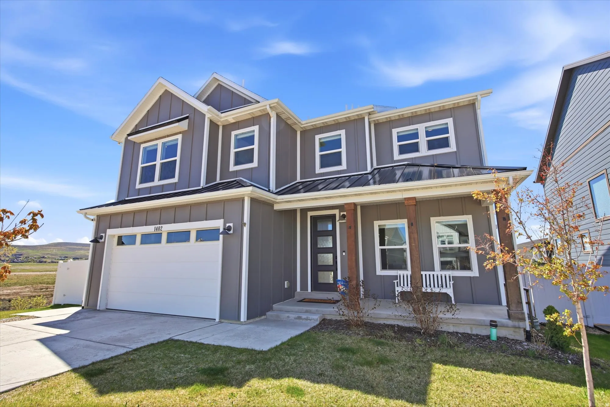Contemporary two-story residence with gray board and batten siding, white trim, and a black metal roof accent