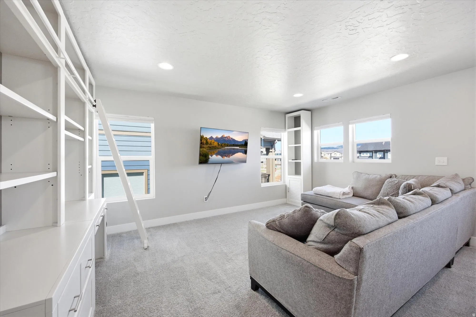 Carpeted room featuring built-in white shelving with a rolling ladder, a built-in desk, and recessed lighting