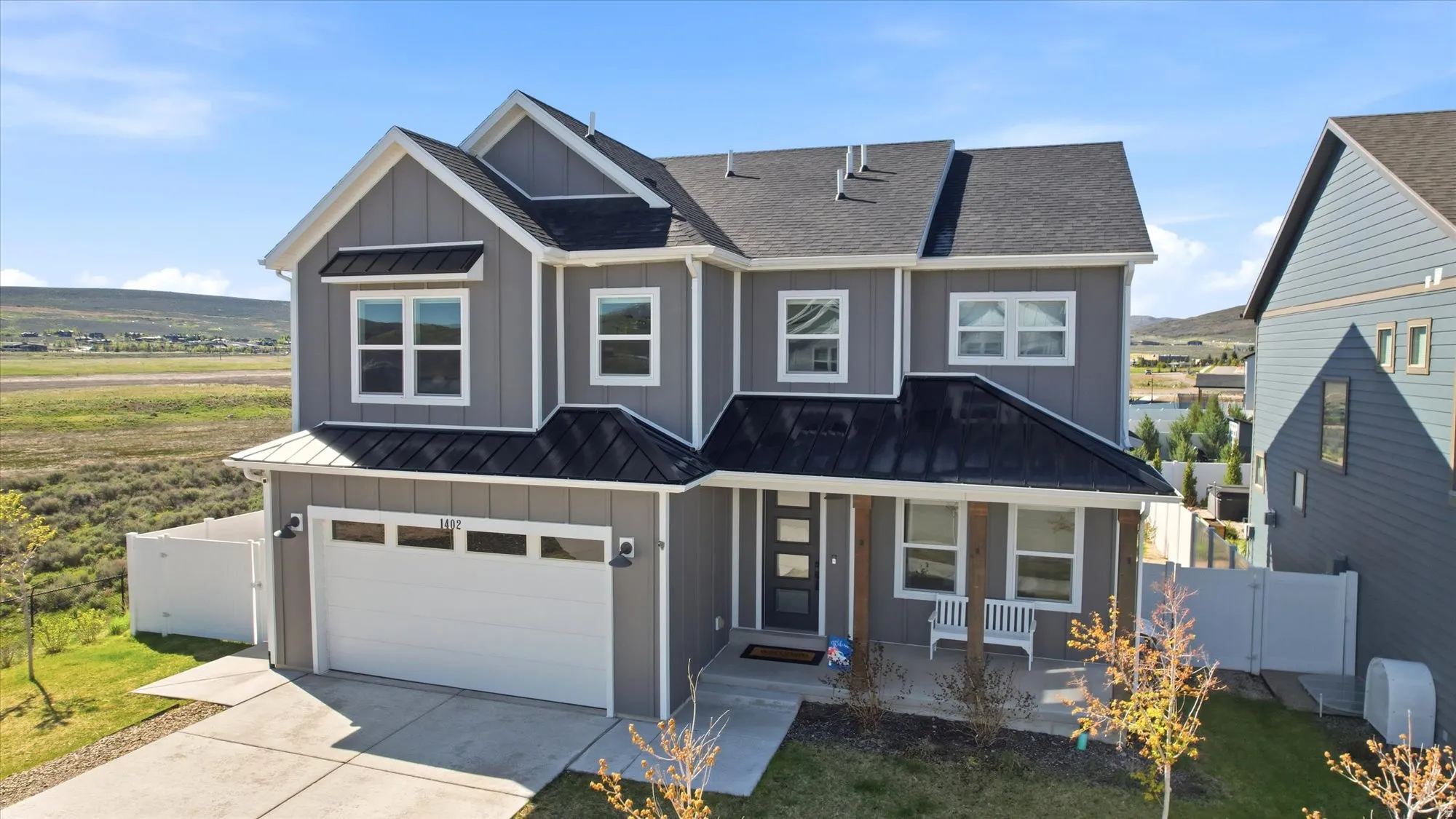 Contemporary gray siding residence with prominent gables, a black metal accent roof over the entry, an attached two-car garage, a concrete driveway, and a covered porch