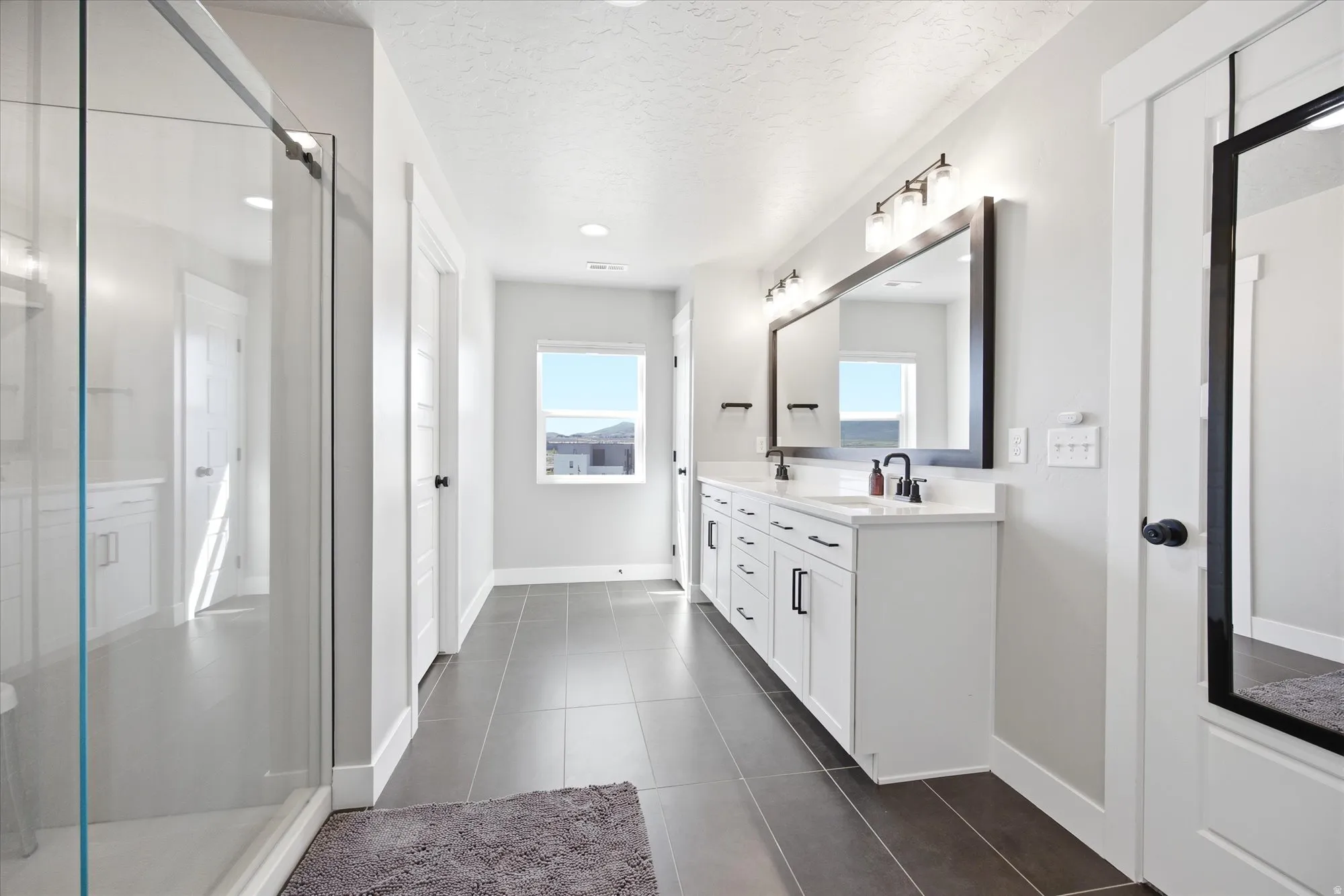Spacious bathroom featuring a dual vanity with white cabinetry, black hardware, and an expansive mirror