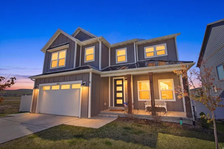 Modern two-story residence with gray board and batten siding, a white garage door, and a covered porch supported by wood-finish pillars