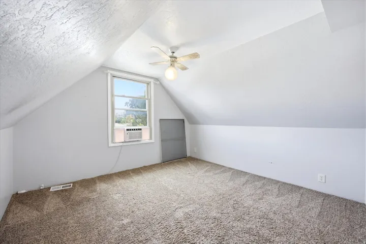 Carpeted room with sloped ceilings, a window, and a ceiling fan