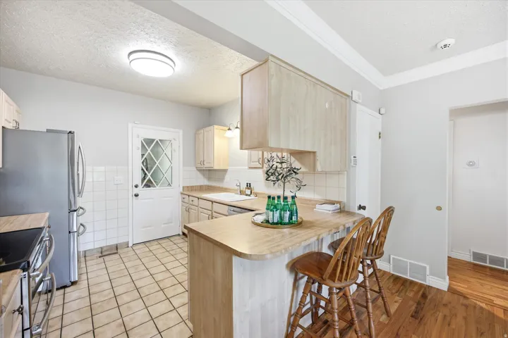 Kitchen featuring a breakfast bar, light wood-finish cabinetry, tile flooring, stainless steel refrigerator, and a door with diamond-patterned lites
