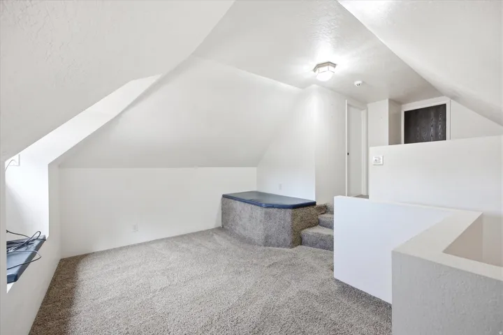 Carpeted attic space featuring sloped ceilings, a built-in carpeted platform, and an overhead lighting fixture