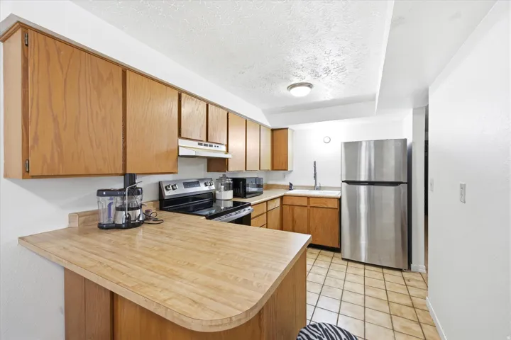 Kitchen featuring abundant wood-finish cabinetry, a stainless steel refrigerator, black and stainless steel range, and tile flooring