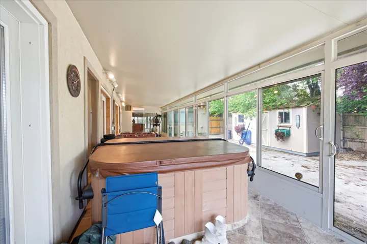 Enclosed patio featuring a spa with a wood-finish cabinet, full-length windows, ceramic tile flooring, and a shed exterior