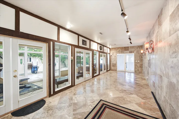 Spacious interior corridor featuring natural stone tile flooring, a stone accent wall, and multiple sets of glass-paneled double doors
