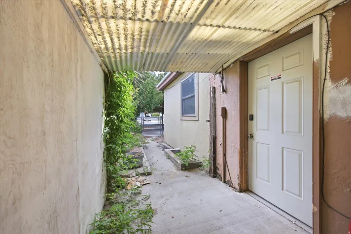 Covered walkway with a corrugated metal roof, concrete pathway, and panel-style entry door