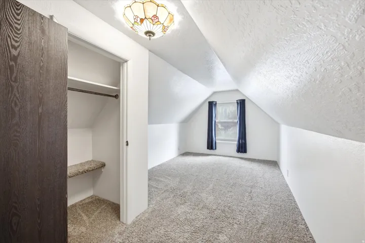 Attic room featuring sloped ceilings, light-hued carpeting, and a window with dark curtains
