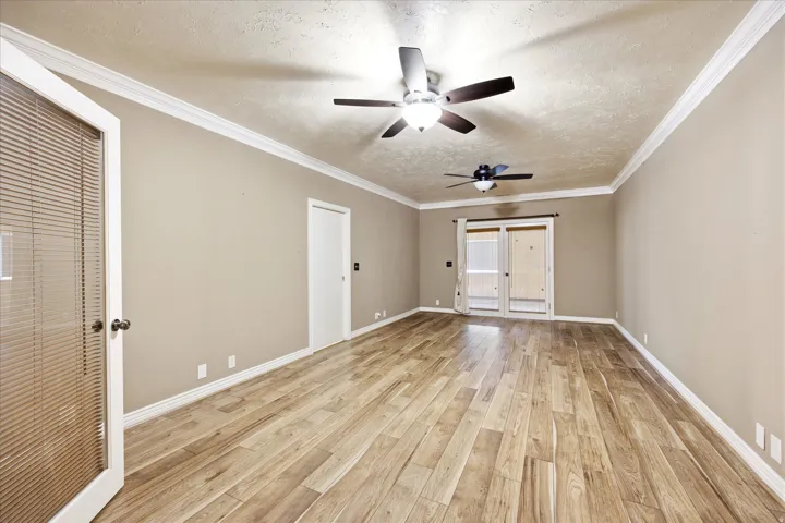 Spacious room featuring wood-finish flooring, two ceiling fans with integrated lighting, crown molding, and neutral wall tones