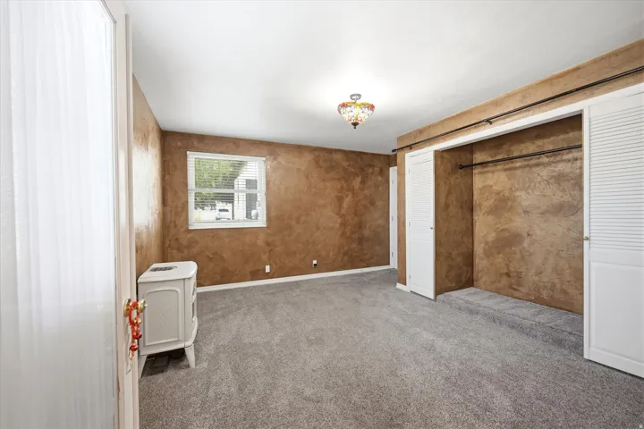 Carpeted room featuring a window with blinds, a decorative ceiling fixture, and a built-in closet with bi-fold doors