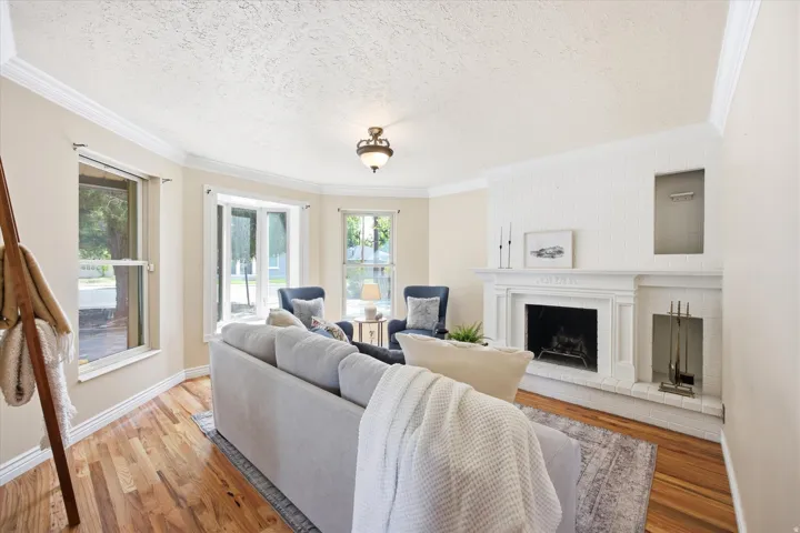 Living area featuring a white painted brick fireplace with a decorative mantel, wood-finish flooring, and multiple windows