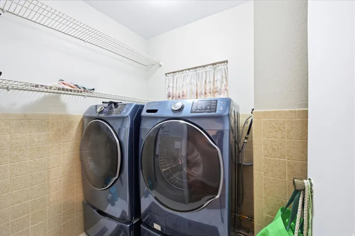 Laundry area featuring neutral-toned tile wainscoting and convenient wire shelving