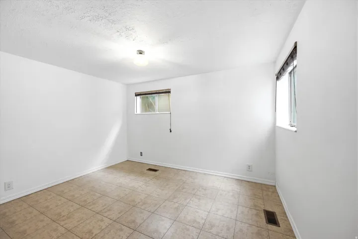 Spacious room featuring tile flooring, white walls, and two windows providing natural illumination