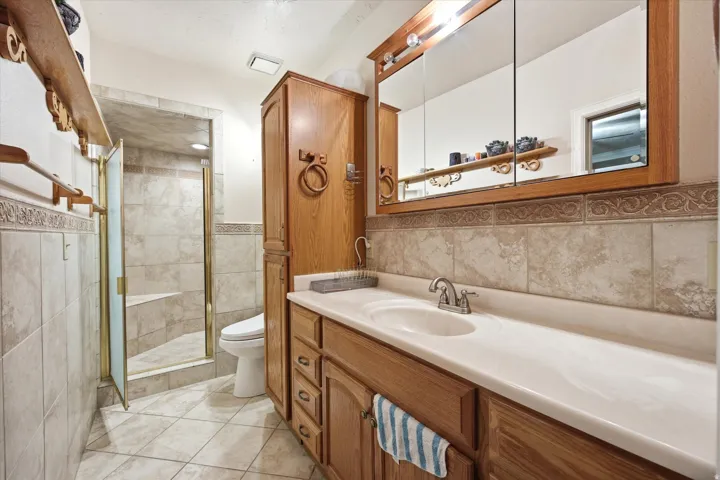 Bathroom featuring an integrated sink vanity with wood-finish cabinetry, a large mirrored medicine cabinet, and a tiled shower with a built-in bench