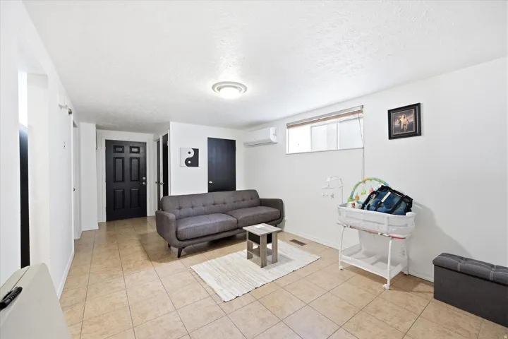 Bright living area featuring neutral tile flooring, white walls, a black paneled door, and a horizontal window with blinds