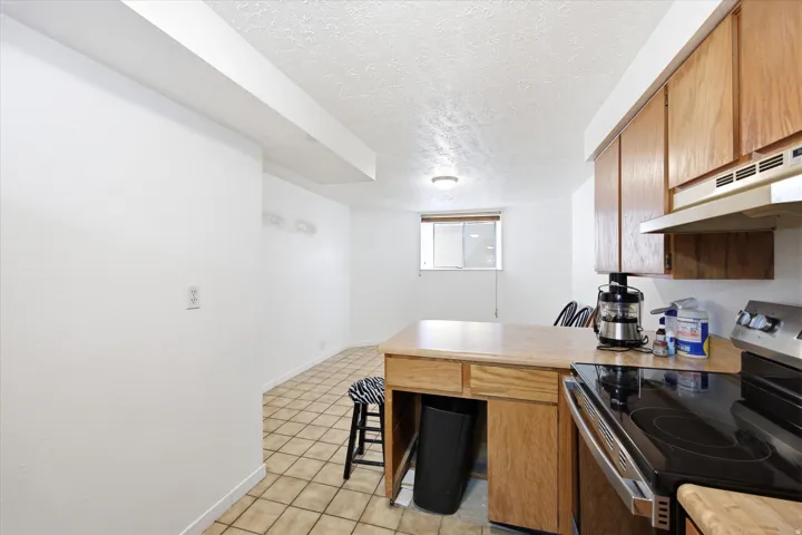 Kitchen area featuring wood-finish cabinetry, a stainless steel electric range, and light-toned tile flooring