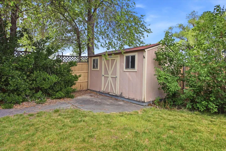 Storage shed featuring dual windows, double doors with cross-brace detailing, and a concrete pad