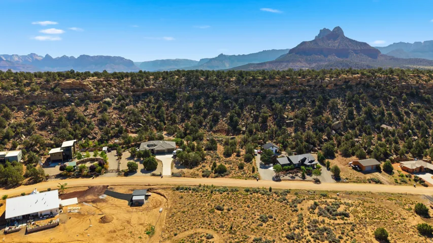 Expansive desert landscape featuring multiple properties, rugged terrain, and distant mountain formations under a clear blue sky