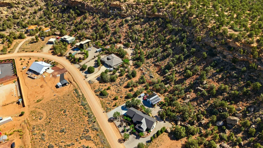 Expansive desert landscape featuring multiple properties, winding dirt roads, and a backdrop of natural rock formations and abundant natural vegetation