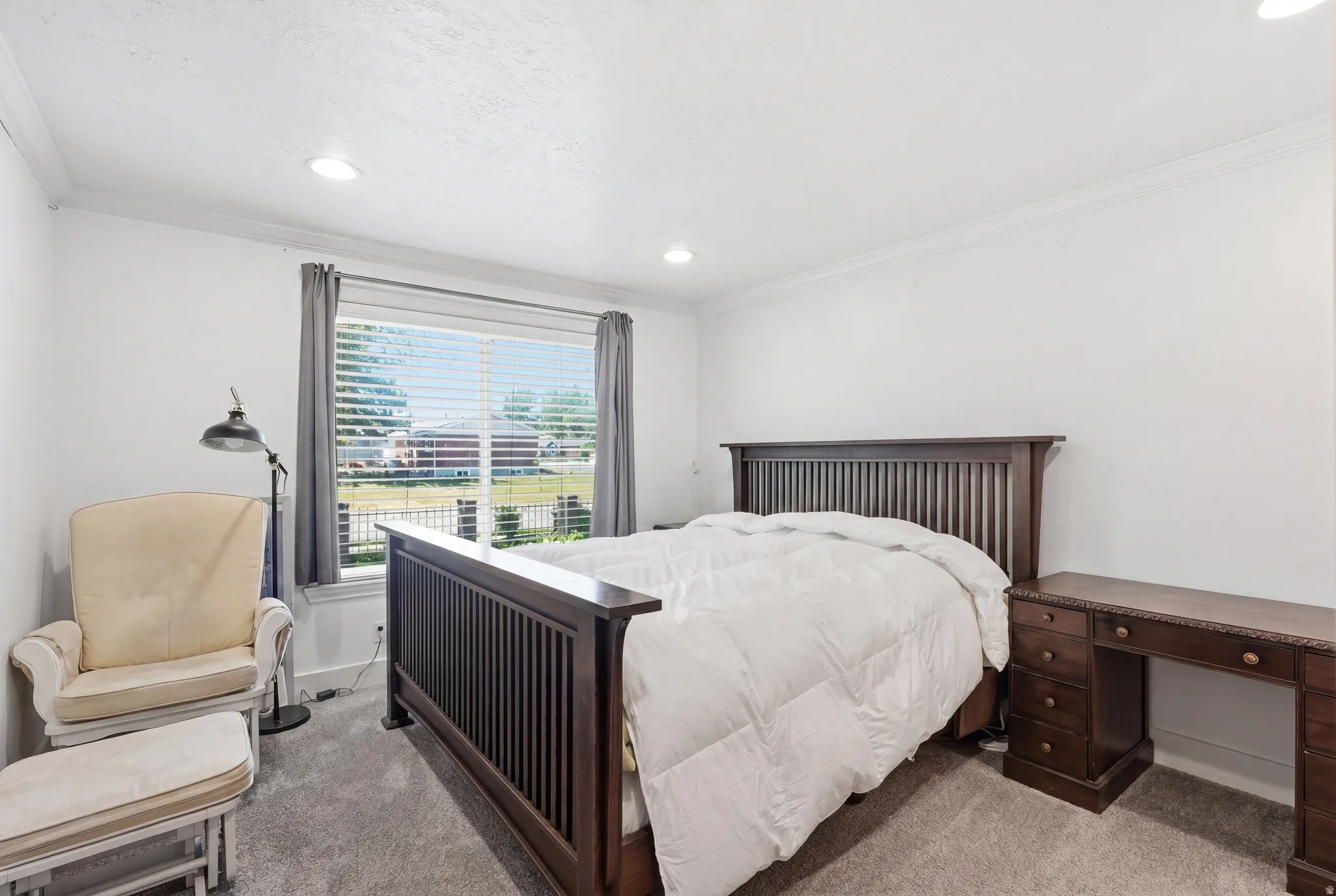 Spacious bedroom featuring clean white walls, recessed lighting, crown molding, and plush gray carpeting