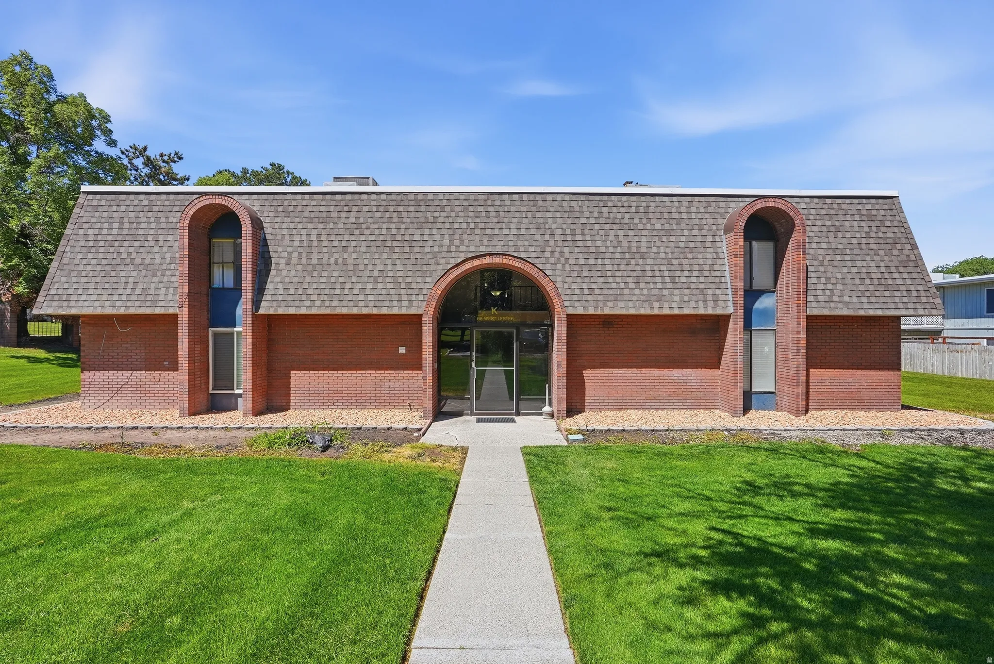 Brick facade building with an arched entryway and matching dormers, set amidst a vibrant green lawn and a concrete walkway