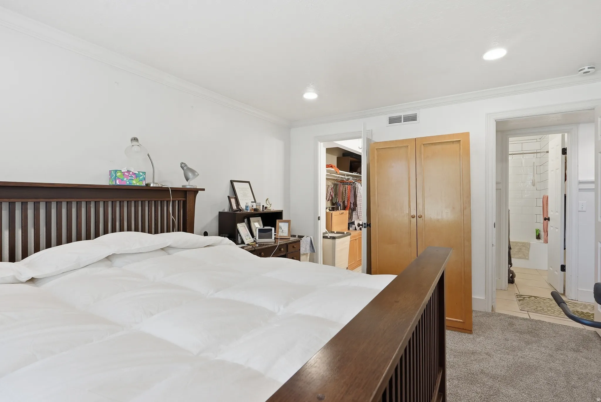 Carpeted bedroom featuring recessed lighting, crown molding, a built-in closet with double doors, and a bathroom with tiled flooring